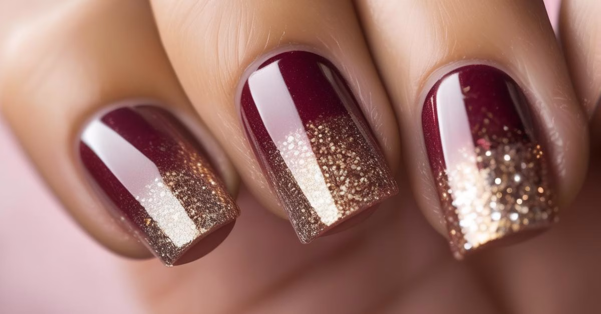 Zbliżenie dłoni z bordowymi paznokciami w kształcie zaokrąglonych kwadratów, ze zdobieniem ombre i złotymi akcentami.